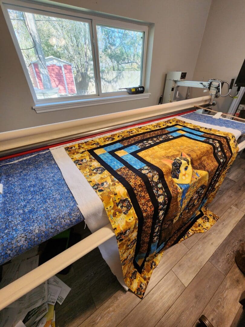 A colorful quilt in progress on a quilting frame near a window.